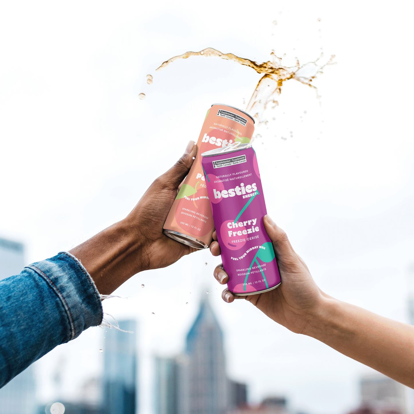 Two hands holding 'besties' energy drinks with a cityscape in the background